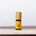 A 10ml amber glass bottle of Ylang Ylang essential oil with a wooden cap next to its yellow packaging box.