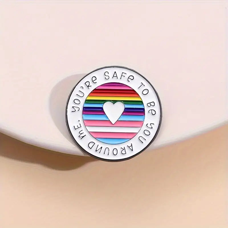 Round pin featuring a rainbow background, a white heart in the center, and the text You are safe to be you around me.