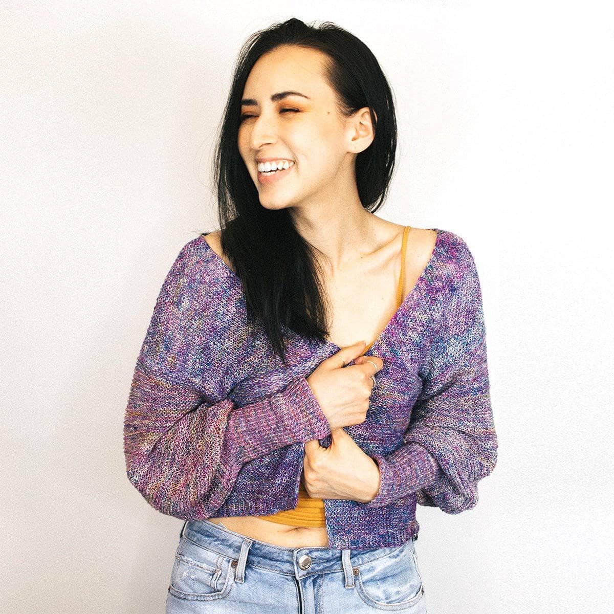 A woman wearing a vibrant, multicolored, cropped knit V-neck cardigan with long sleeves in a bohemian, artisan style.