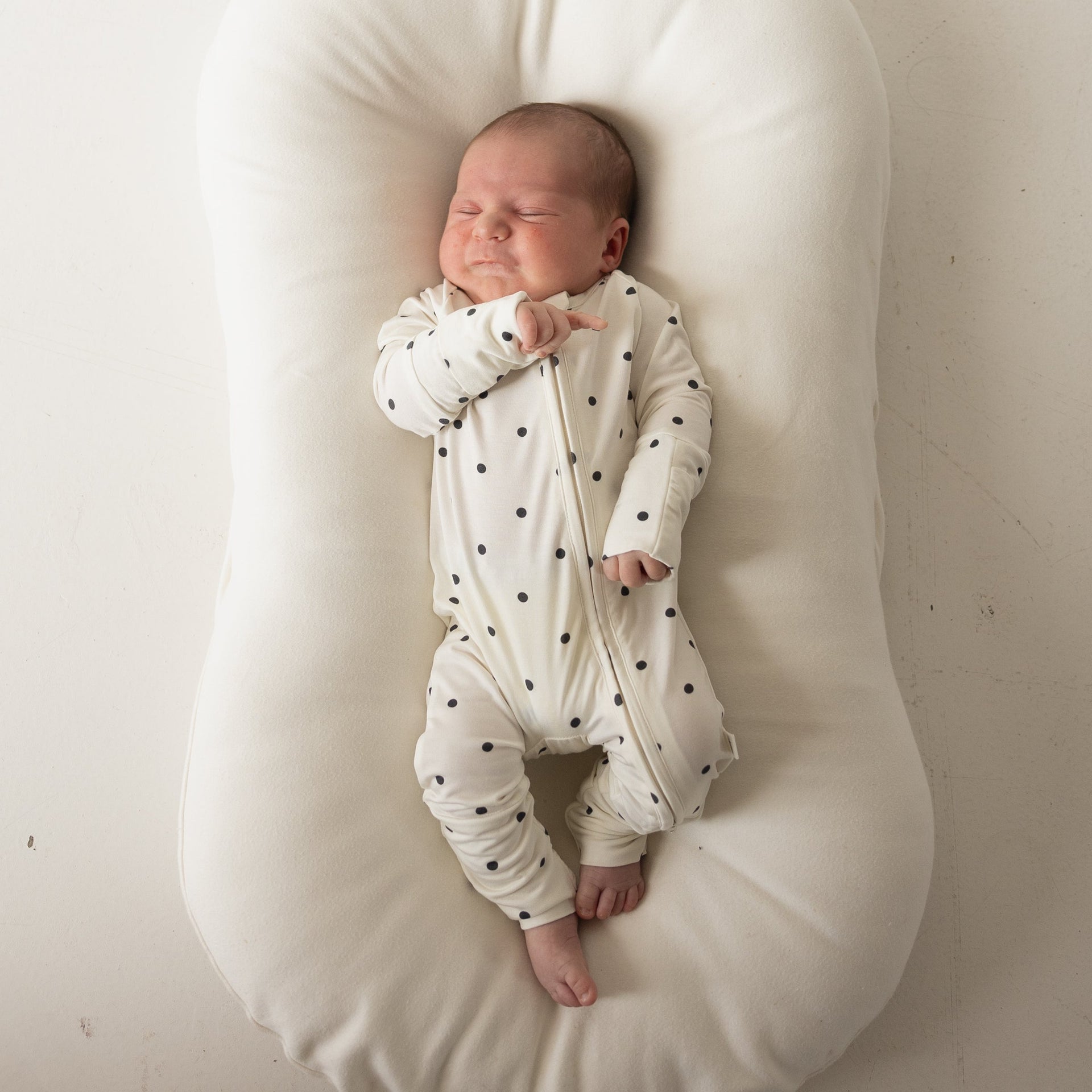 Baby wearing Annie bamboo zip pajamas in creamy off-white with charcoal polka dots