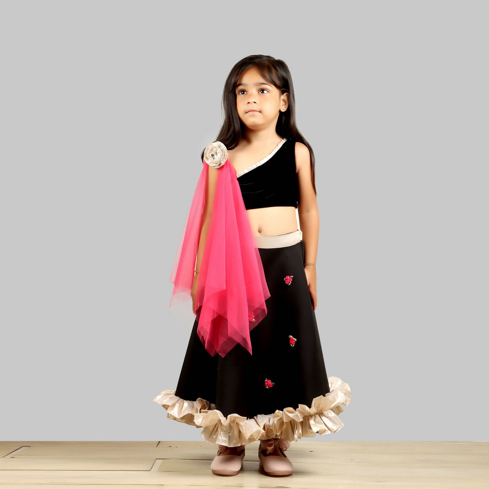 One-shoulder black scuba ghagra choli with gold frill hem and pink floral net dupatta.