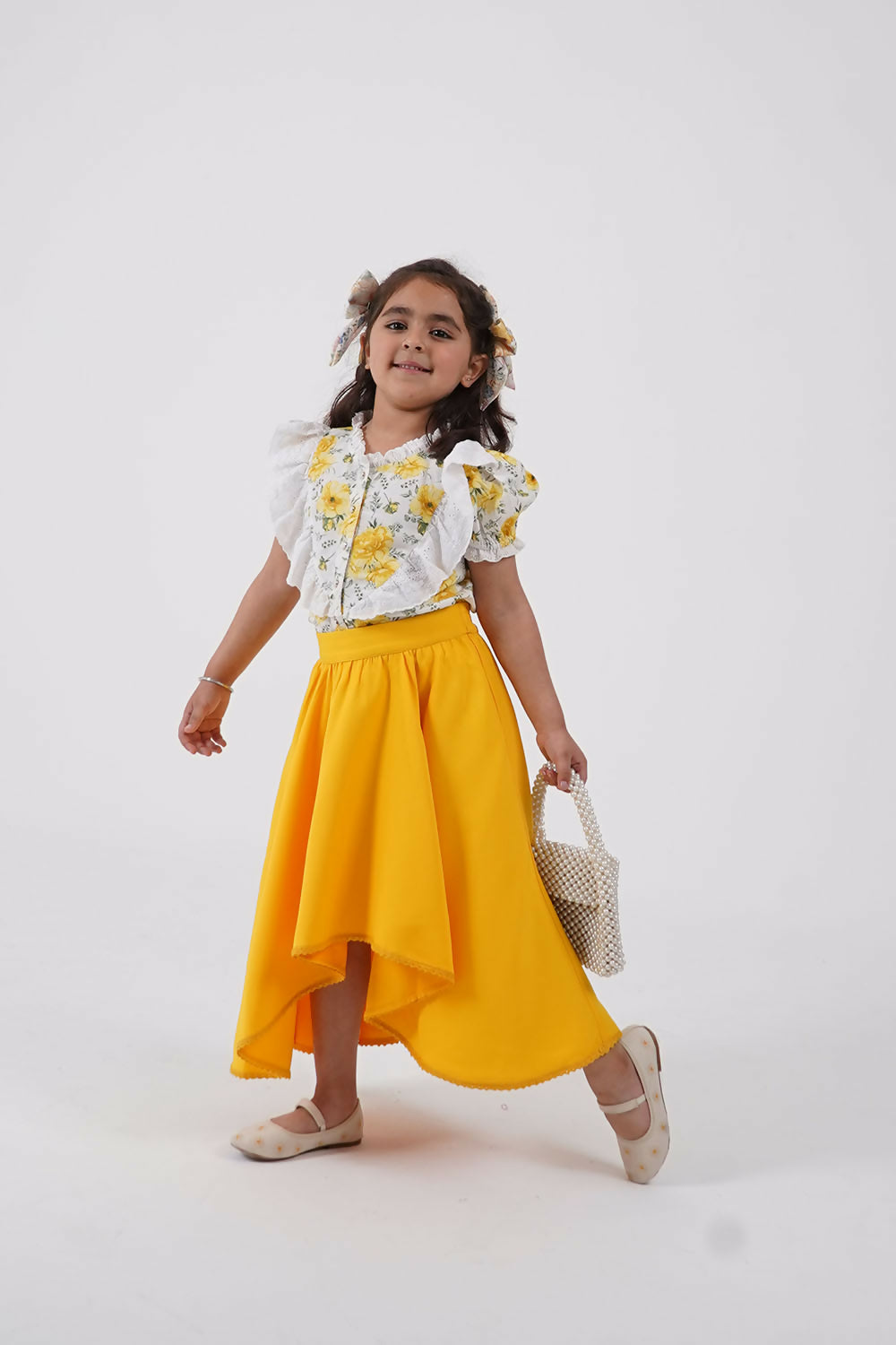 A girl wearing a floral puff sleeve top and a yellow and white high-low flared skirt co-ord set.